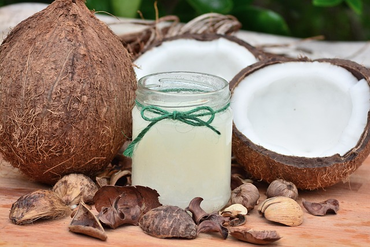 Coconut oil in a jar placed on a table outdoors with a half split coconut placed on one side and full coconut placed on other side.