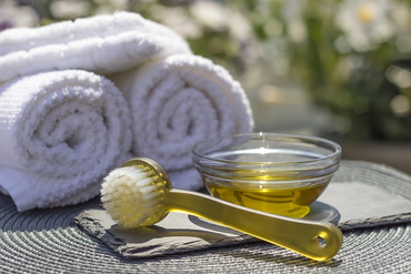 body oil in glass bowl placed outside next to folded towels and brush