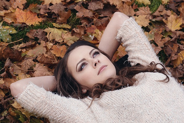 beautiful woman in white sweater lying down on leaves looking at sky.