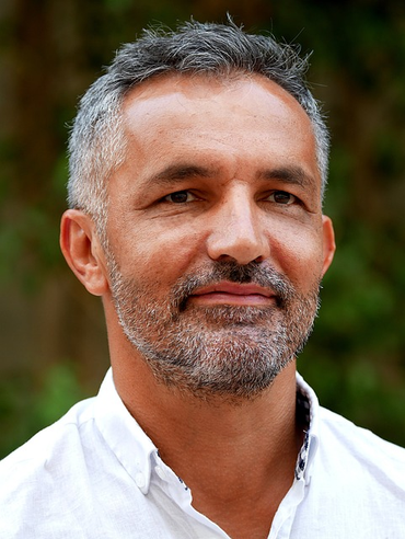 A portrait photo of a middle aged man with grey hair wearing a white shirt.