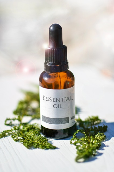 A bottle of essential oil placed on a table surrounded by some green leaves.